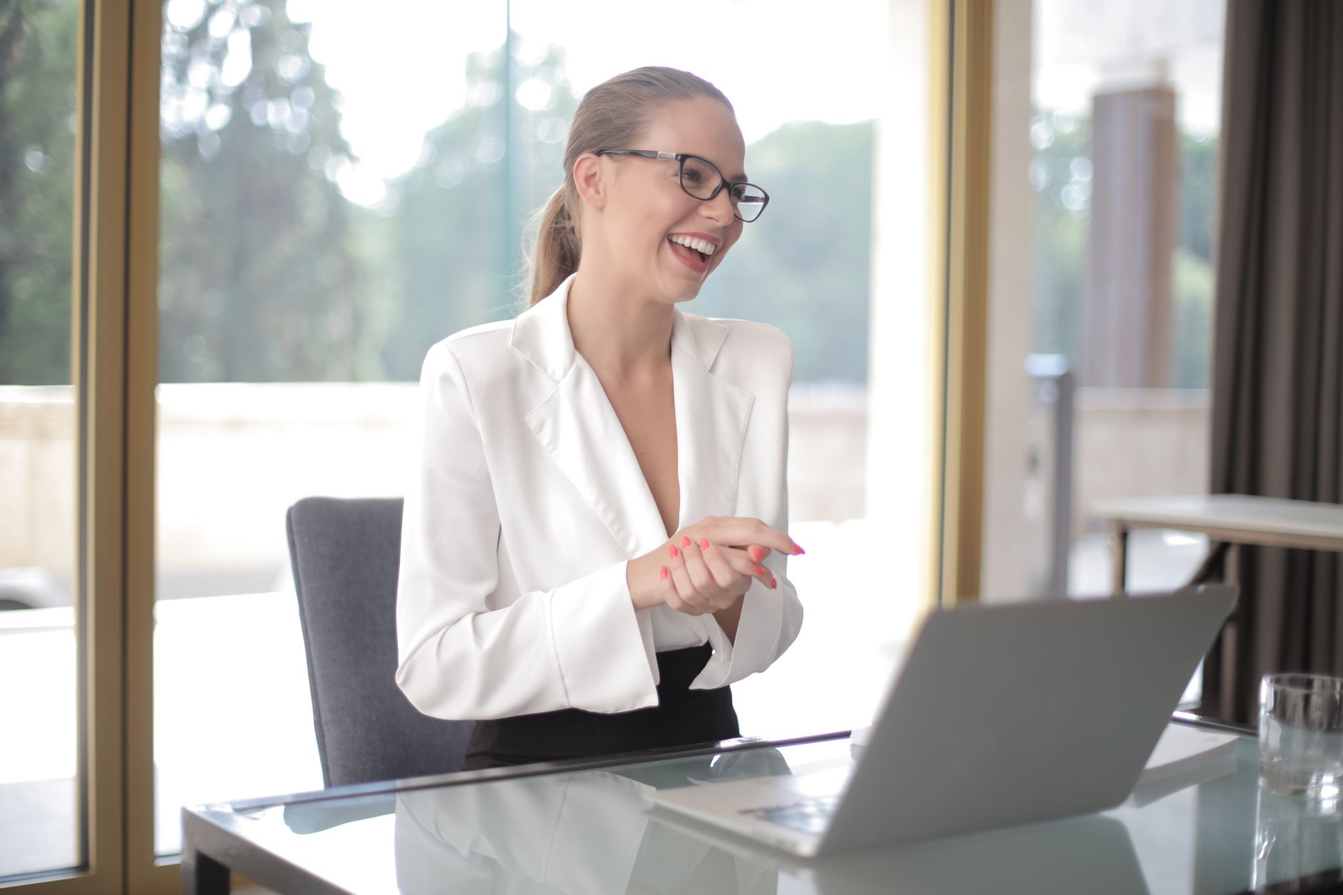 Mujer emprendedora con lentes trabajando con laptop y documentos en una oficina moderna.